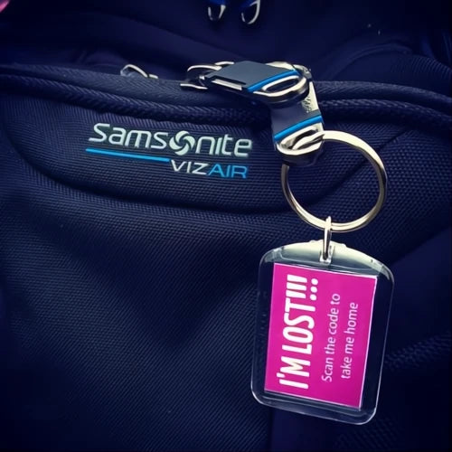 A pink keyring with the text 'I'm Lost' attached to a piece of luggage, with a visible part of the text 'Samsonite Viz Air' on the luggage.