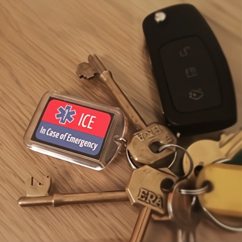 A set of keys with a keyring that has 'ICE In Case of Emergency' labeled on it, placed next to a car key and a house key on a wooden surface.