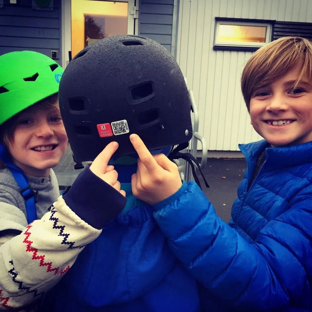Two children holding a black helmet with a QR code, smiling.